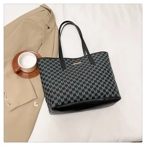 Detail of grey M-letter pattern tote bag with black leather base and gold metal logo