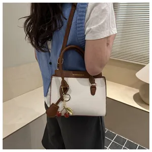 Détail du sac à main bicolore avec pendentif cerise et texture de la poignée en cuir