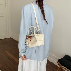 Mini borsa a secchiello crema con tracolla e ciondolo a orsetto vista sul modello
