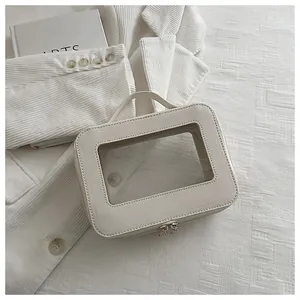 Macro view of cream vanity bag featuring a clear window and metallic double zippers