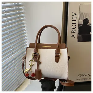 Détail du sac en cuir litchi blanc avec poignées marron et breloque cerise en métal