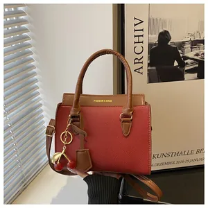 Détail du sac à main rouge et marron avec pendentif cerise dorée et texture cuir grainé