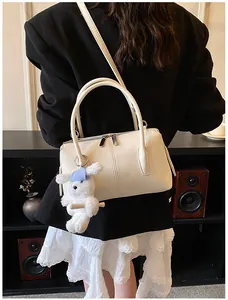 Detail of white leather Boston bag with plush bunny charm worn by a model