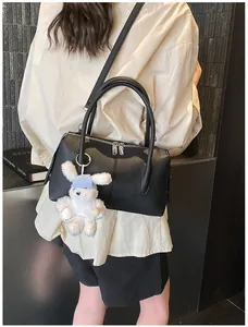 Detail of black pebbled leather handbag with adjustable strap and plush rabbit charm