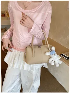 Detail view of beige leather satchel featuring a cute plush bunny charm on the side