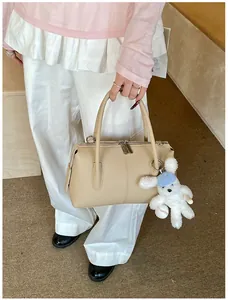 Close-up of beige lychee texture leather boston bag with a cute plush dog pendant charm