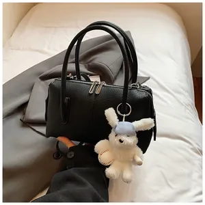 Detail of black lychee leather handbag with silver zippers and a cute plush bunny charm