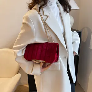 Detail einer dunkelroten Samttasche mit Goldkette, getragen von einem Modell in Beige