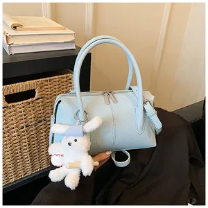 Detail of light blue crossbody bag with lychee texture and a cute bear bag charm