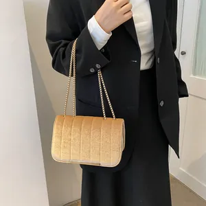 Detail der goldbraunen Samt-Umhängetasche mit Kette, getragen zu einem schwarzen Blazer