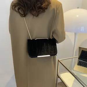 Detail einer schwarzen Samt-Umhängetasche mit Goldkette und Metallsteg auf einem Blazer