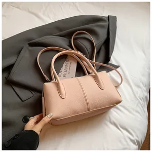 Close-up of pink litchi grain leather handbag with stitching details on a white bed