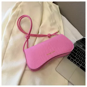 Close-up of bright pink faux leather shoulder bag with crocodile texture and gold text