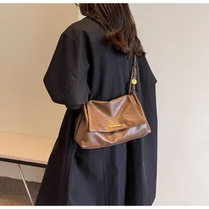 Brown leather shoulder bag with gold chain strap shown on a model's shoulder