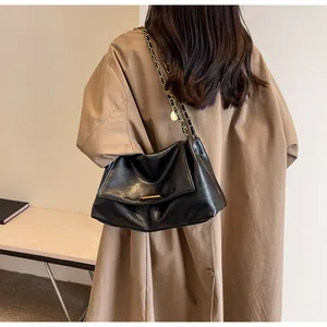 Detail view of black leather shoulder bag with gold chain strap on a camel coat