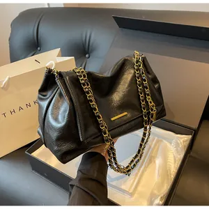 Detail of the black leather shoulder bag showing the gold chain strap and metal clasp
