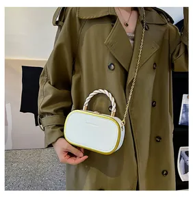 Detail of white box handbag with twisted handle and golden chain strap on khaki coat
