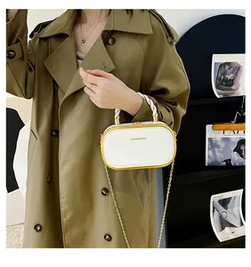 White box crossbody bag with yellow trim and gold chain held by model in trench coat