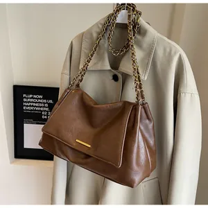 Close-up of brown lychee texture leather bag with gold chain strap on a beige coat