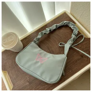 Detalle de bolso de hombro fruncido verde claro con bordado de mariposa rosa suave