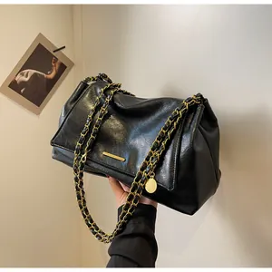 Detail of soft black PU leather handbag with gold chain strap and metallic hardware