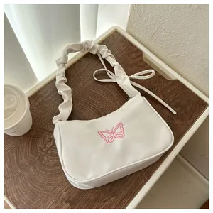 Detalle de bolso blanco con bordado de mariposa rosa y correa con volantes