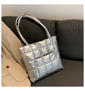 Detailed close-up of shiny silver quilted tote bag with metallic texture on a grey sofa