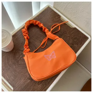 Detalle de bolso naranja con bordado de mariposa rosa y asa con diseño de pliegues
