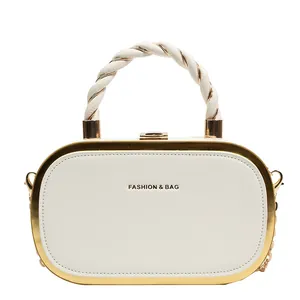 Detail of elegant cream-white box clutch with gold metal frame and twisted handle design