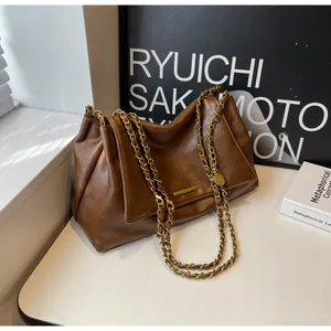 Detail of dark brown leather handbag featuring textured grain and gold chain shoulder straps