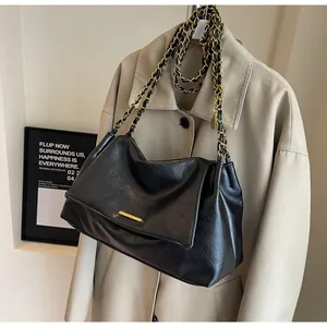 Close-up of black leather handbag with gold metal bar and chain strap detail