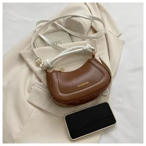 Détail d'un sac sous le bras demi-lune marron avec sangle blanche et accents dorés
