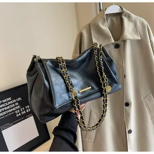 Detail of black pleated faux leather bag featuring dual gold chains and metal hardware