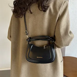 Détail d'un sac bandoulière noir en cuir avec poignée nouée porté sur un manteau marron chic