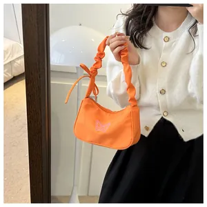 Detalle de bolso naranja de nailon con bordado de mariposa y asa fruncida estilo suave