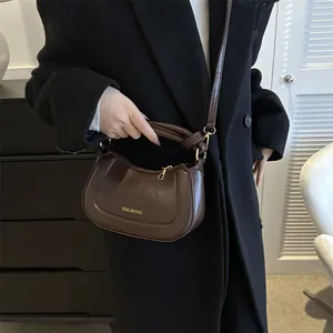 Sac demi-lune en cuir marron foncé avec logo doré porté en bandoulière par un mannequin