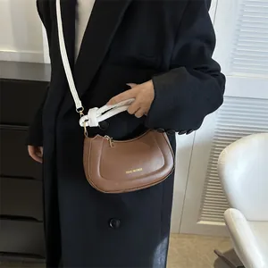 Sac demi-lune en cuir marron avec large bandoulière blanche nouée porté à l'épaule