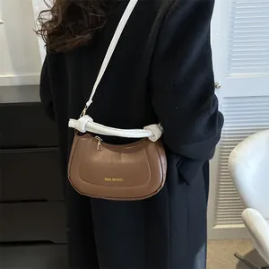 Détail d'un sac demi-lune marron avec poignée nouée blanche et zip en métal doré brillant