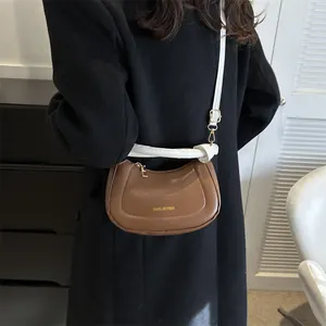 Sac bandoulière demi-lune marron avec logo doré et détail de bandoulière blanche nouée