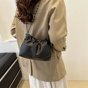 Détail du sac seau noir plissé avec bandoulière en chaîne argentée sur un mannequin