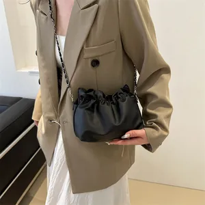 Détail du sac seau noir plissé avec bandoulière chaîne sur un blazer beige élégant