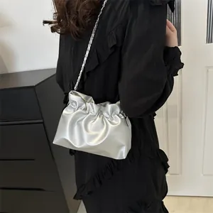 Sac seau argenté avec design plissé et chaîne en métal porté à l'épaule par le mannequin