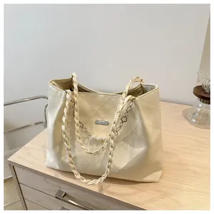 Close-up of cream quilted tote bag featuring a pearl chain and woven shoulder strap