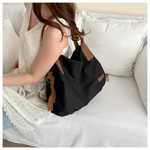 Detail of a large capacity black canvas tote bag with brown woven straps on white sofa