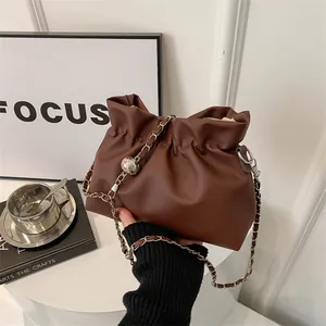Détail d'un sac seau plissé marron avec bandoulière chaîne argentée et breloque boule