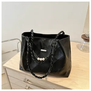 Detail of black quilted tote bag featuring a pearl chain and woven handles on a wooden surface