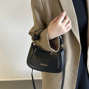 Sac à main bandoulière chic en cuir noir avec poignée nouée porté par un modèle