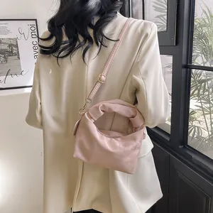 Detail of light pink pleated handbag with twisted handle and gold hardware on model
