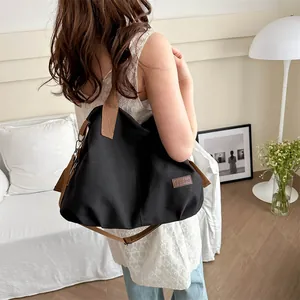 Large capacity black canvas tote bag with brown straps shown on a model in a cozy room