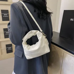 Detail of white pleated cloud bag with thin strap and gold buckle on a grey blazer